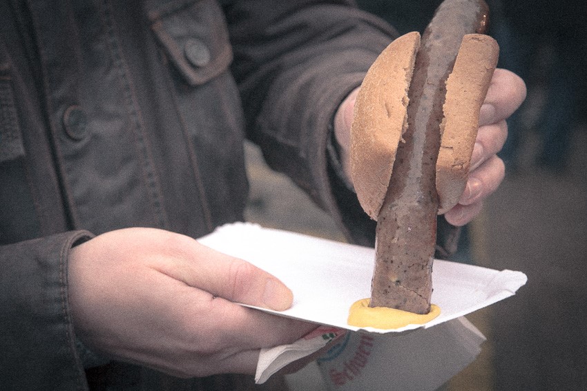 Grainy photo of a "Bratwurst" (Sausage) being dipped into some mustard