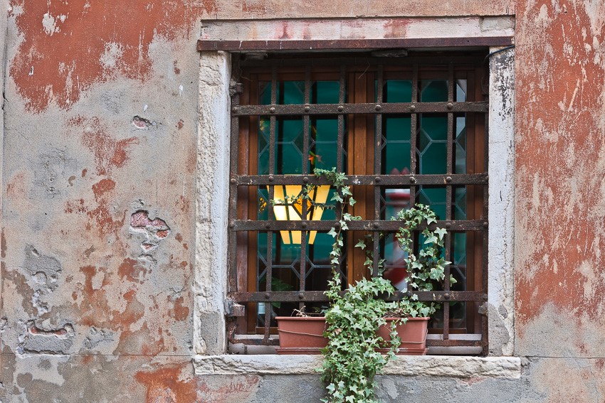 Detail photo of a house and window with chipped off paint and a flower box in the window in Venice, Italy