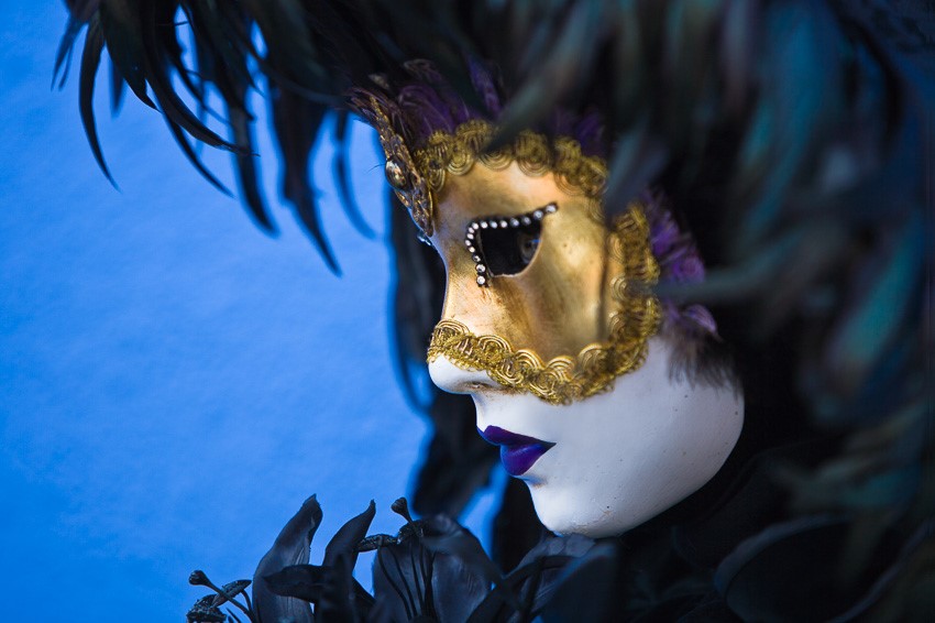 Close-up photo of the golden mask and the black costume of a woman at the carnival in Venice, Italy against a blue background