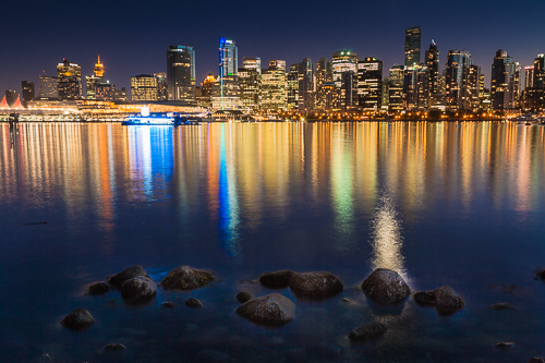 Photo of the illuminated skyline of Vancouver in British Columbia, Canada by night with the lights reflecting in the water